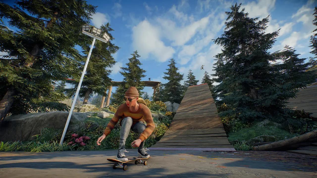 A skater crouched low on a board in a sunny forest plaza with a wooden ramp behind